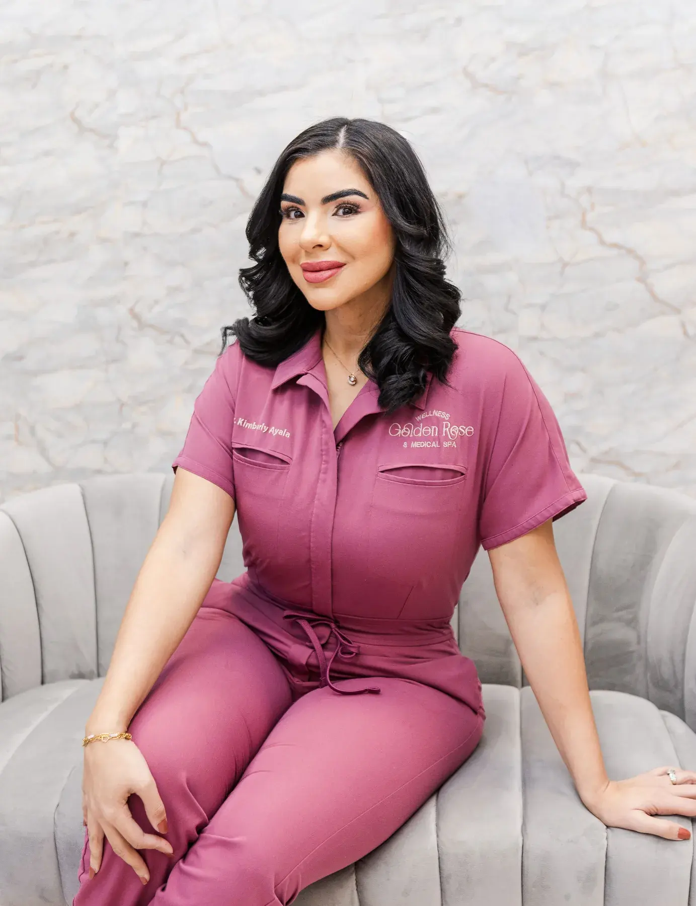 Dr. Kimberly Ayala Vega, DNP, APRN, FNP-C, seated in front of the rose wall at Golden Rose Wellness & Medical Spa